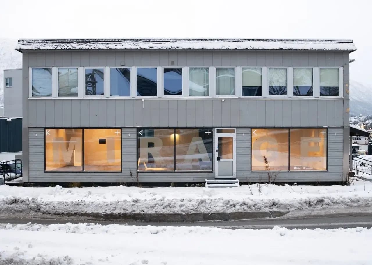 A two-story grey building stands in a snowy setting with the word "MIRAGE" displayed across its large ground-floor windows.